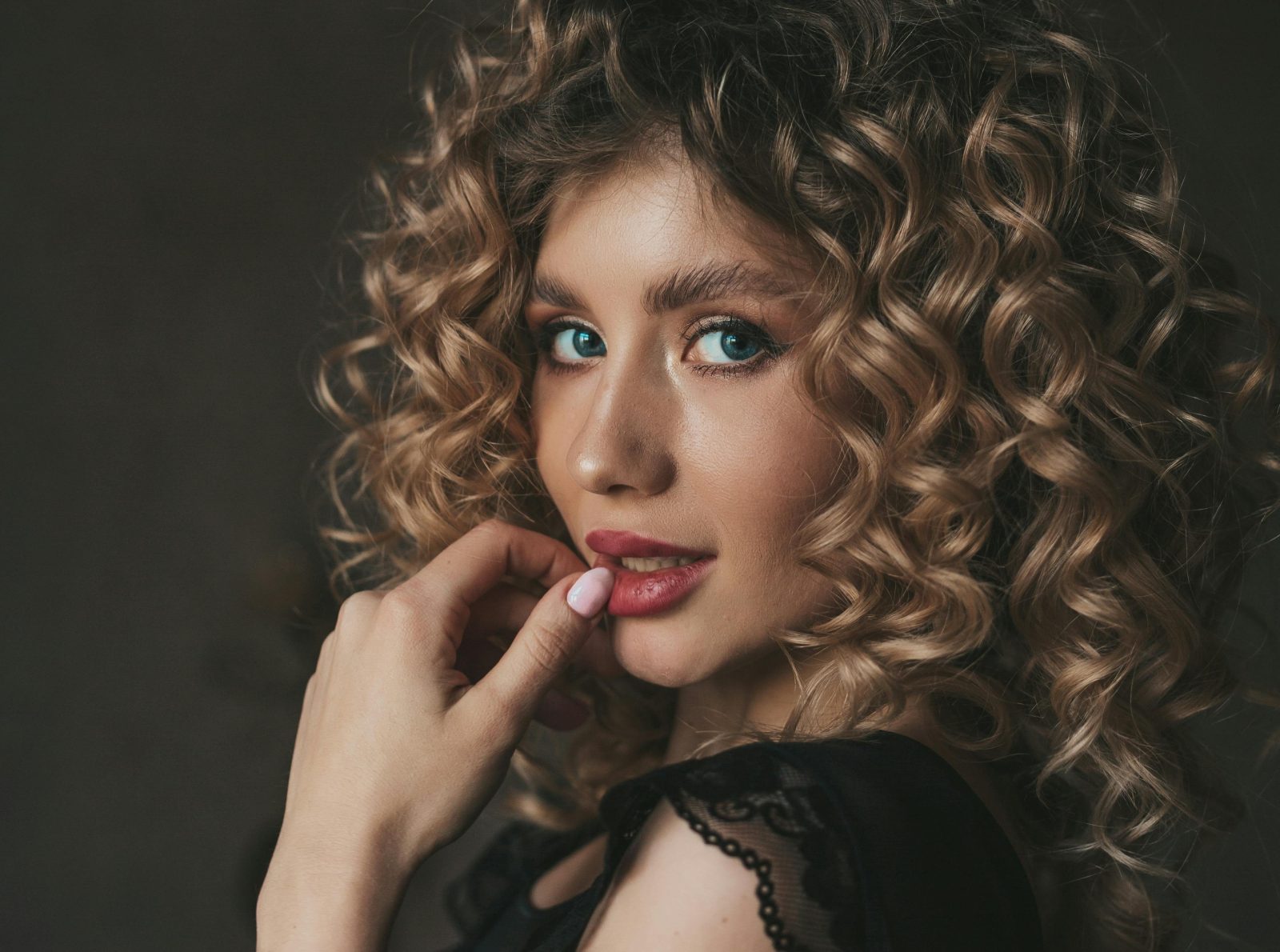 Close-up portrait of a woman with curly hair, blue eyes, and red lips.